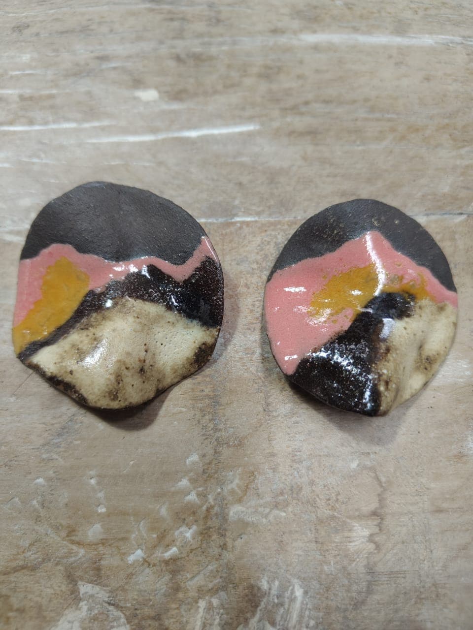 Par de brincos em formato de gota com esmalte em faixas: preto no topo, rosa no meio, mancha amarelo-mostarda e base bege salpicada.
